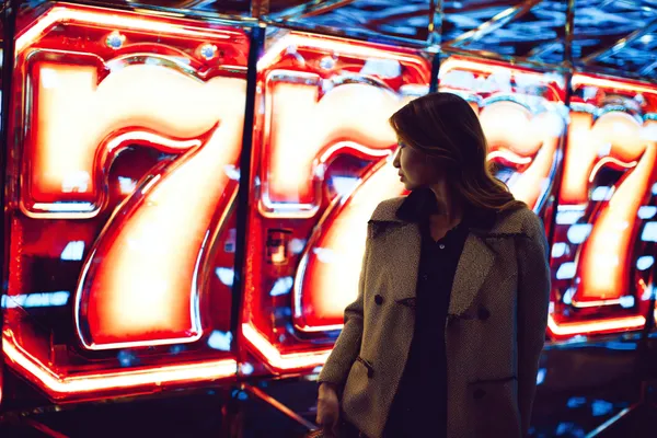 A woman smiling while playing online games on her laptop, surrounded by neon casino elements, showcasing 6777DETT’s diverse game collection.
